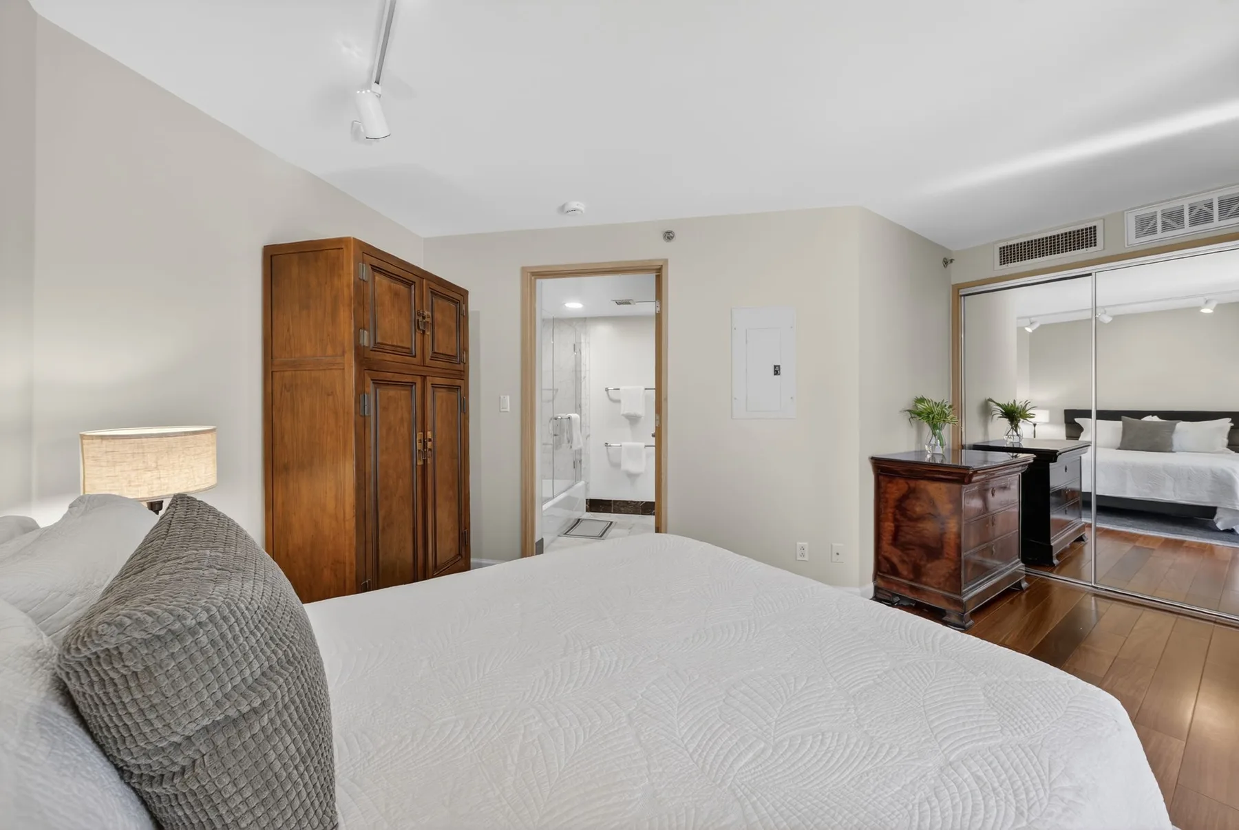 A bedroom with a large bed, a wooden wardrobe, and a bathroom doorway.