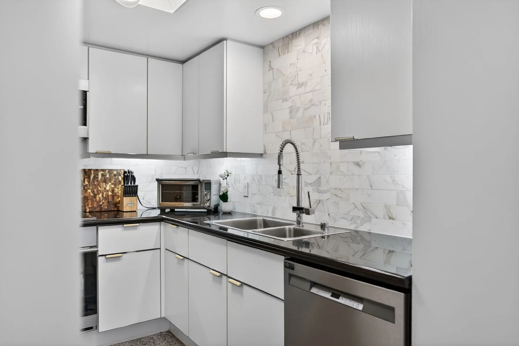 A modern kitchen with white cabinets, dark countertops, and a stainless steel sink.