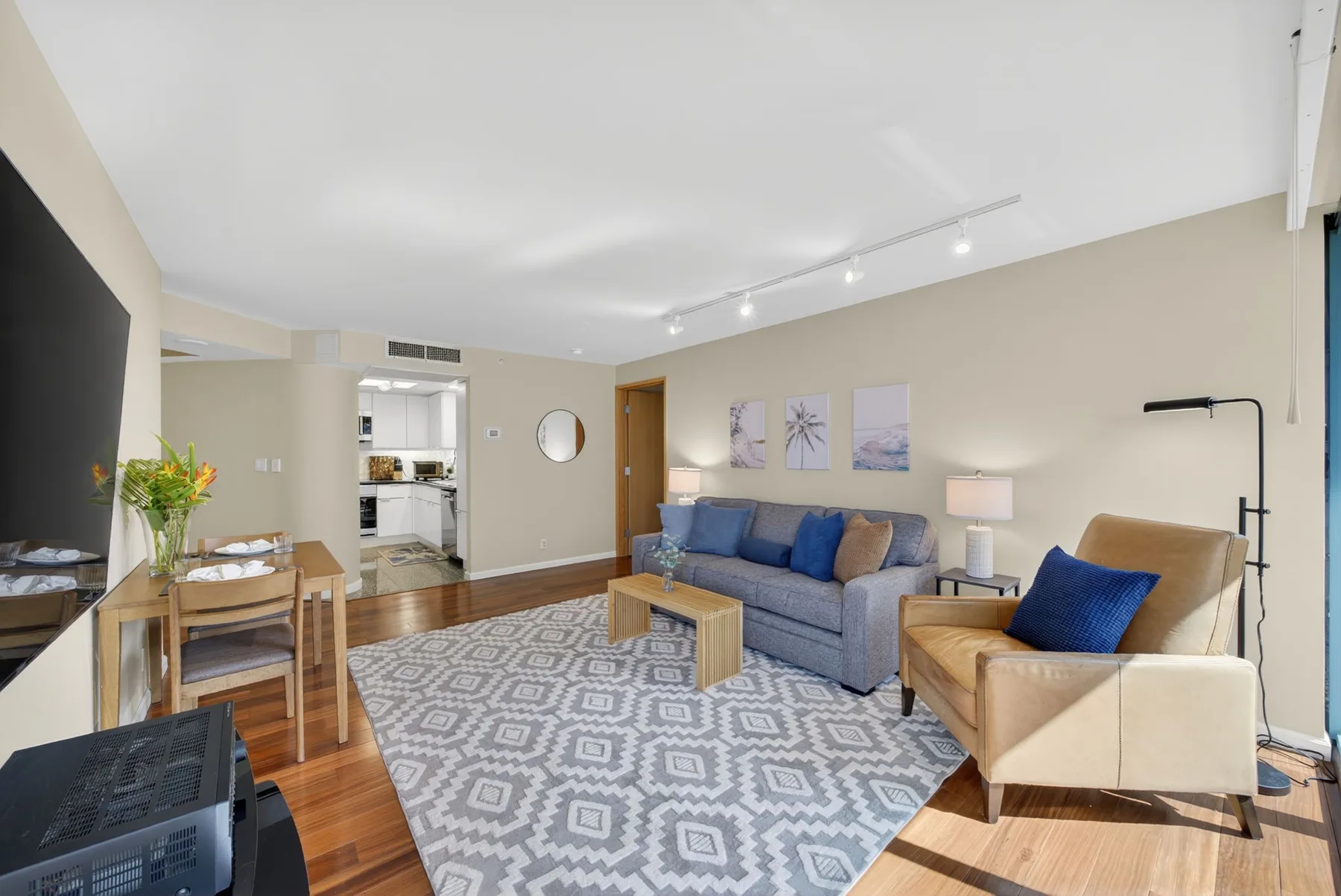 A living room with blue seating, a patterned rug, and a dining area.