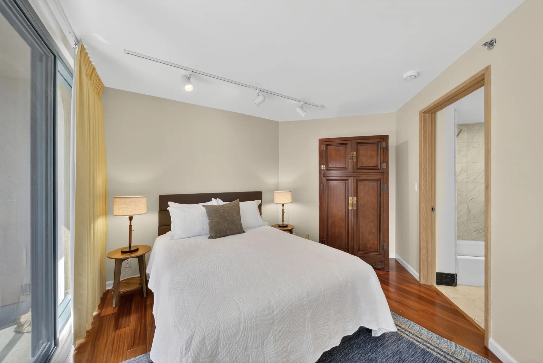 A bedroom with a neatly made bed, bedside tables, and a wooden wardrobe.
