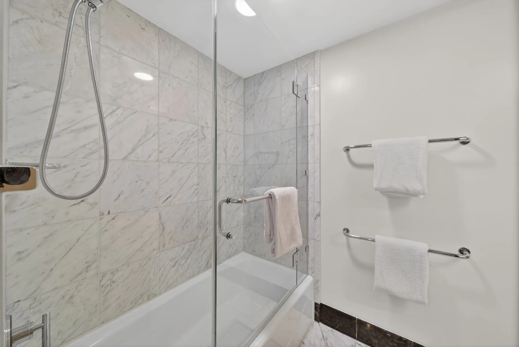 A tiled bathroom with a glass shower screen and towels hanging on rails.