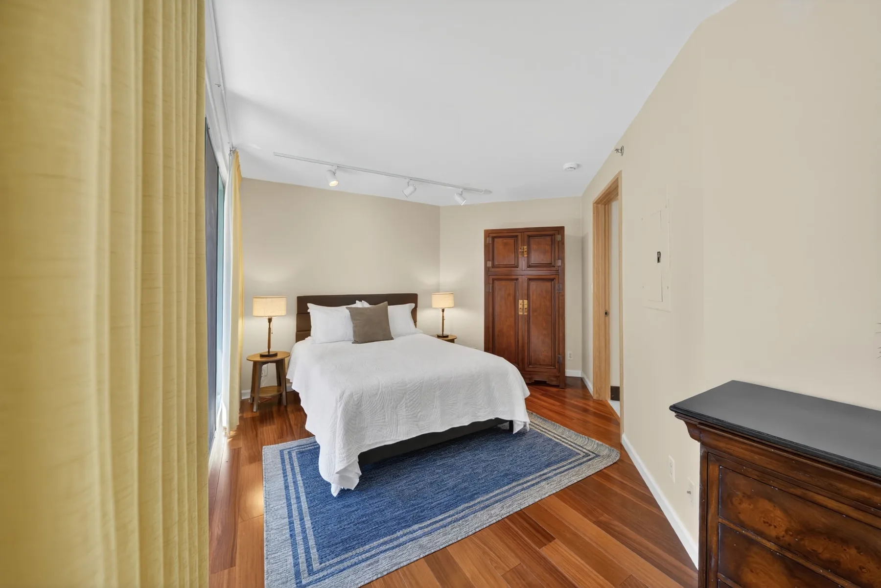 A bedroom with a bed, bedside tables, and a blue rug on the wooden floor.