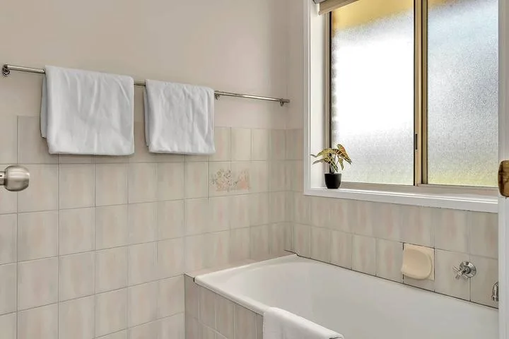Un baño con una bañera bajo una ventana translúcida y toallas en la pared.