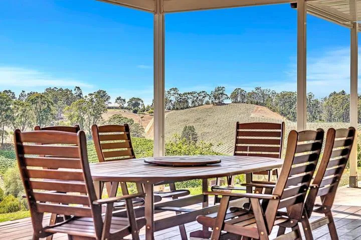 Un comedor exterior cubierto con mesa de madera y asientos frente a colinas onduladas.