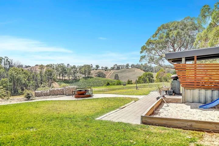 Un patio exterior con césped ofrece vistas a colinas onduladas, junto a un sendero pavimentado y una pequeña zona de juegos.