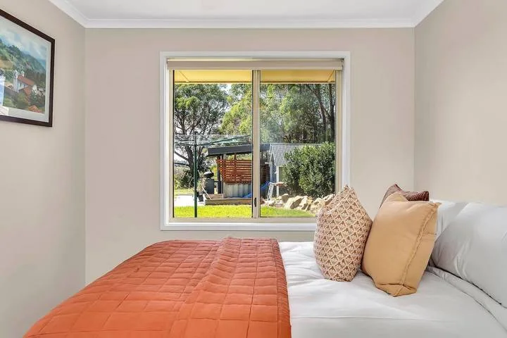 Un dormitorio con una cama junto a una gran ventana con vegetación al fondo.