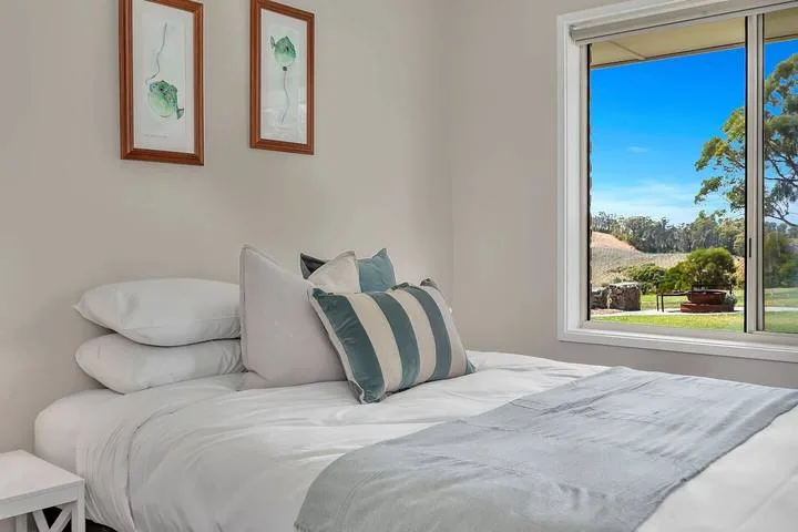 Un dormitorio luminoso con una cama tendida y una ventana grande con vistas a árboles.