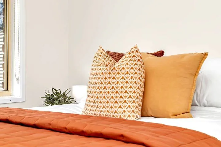 Un dormitorio con almohadas estampadas y ocres sobre una cama.