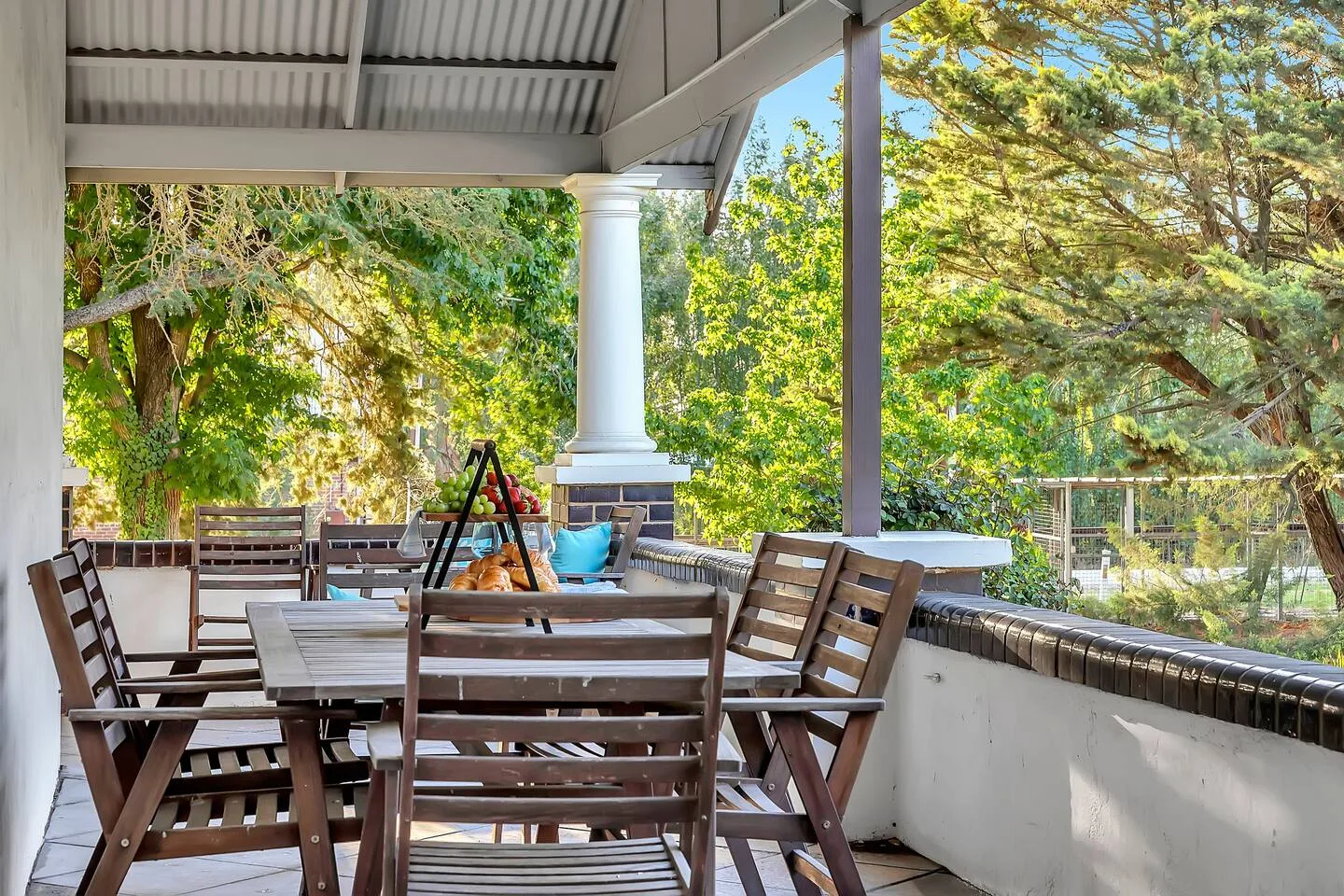 Una zona de comedor exterior cubierta con asientos de madera da a árboles frondosos.