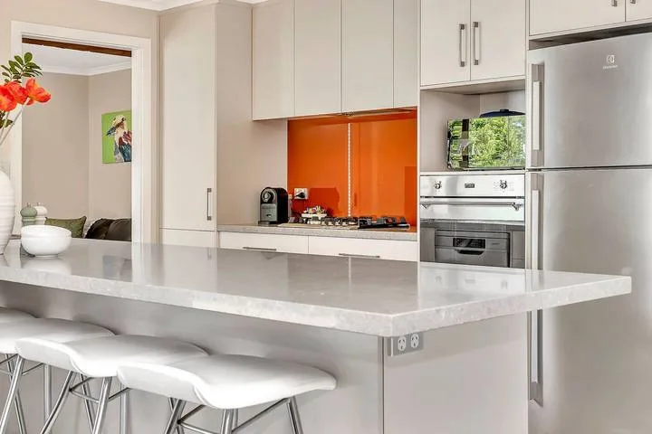 Una cocina moderna con una amplia isla y un salpicadero naranja.