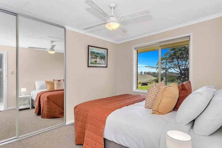 Un dormitorio con una cama vestida de blanco y tonos óxido junto a una ventana amplia.