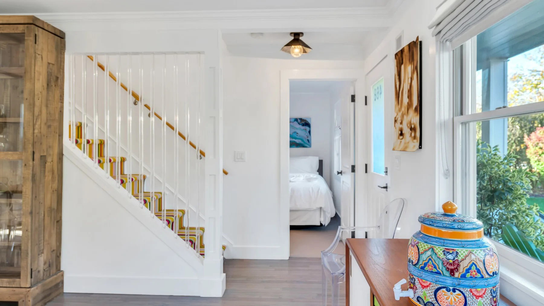 Un pasillo interior luminoso con una escalera y la puerta abierta de un dormitorio.