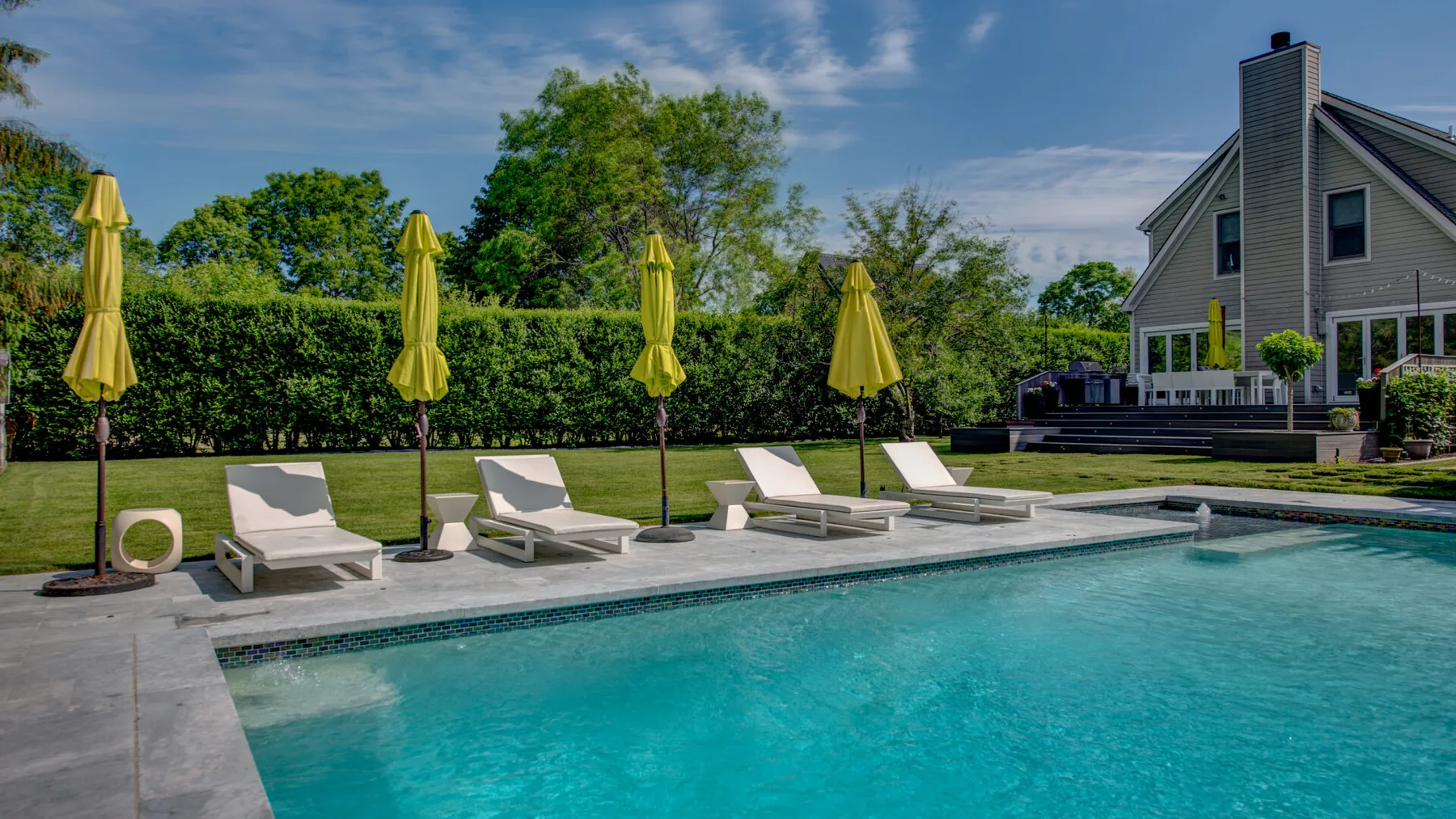Una piscina al aire libre con asientos reclinables y sombrillas cerradas junto a una casa.