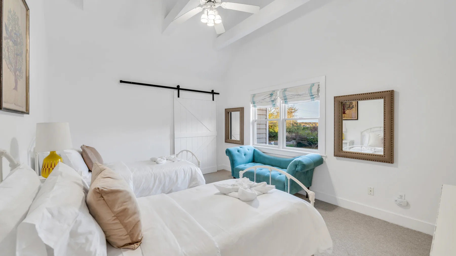 Un dormitorio luminoso con ropa de cama blanca y un asiento turquesa junto a la ventana.