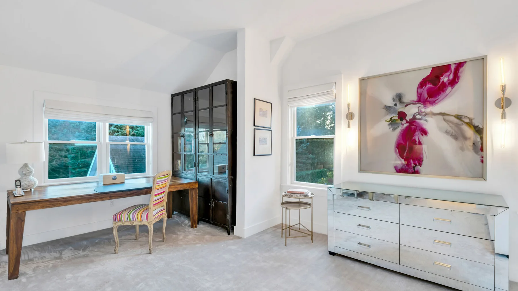 Una habitación luminosa con un escritorio de madera, asientos coloridos y una gran obra floral.