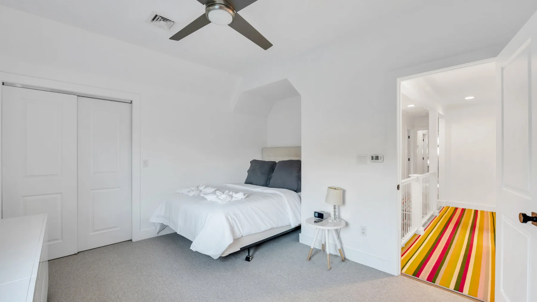 Un dormitorio luminoso con una cama junto a una puerta que da a un pasillo a rayas.