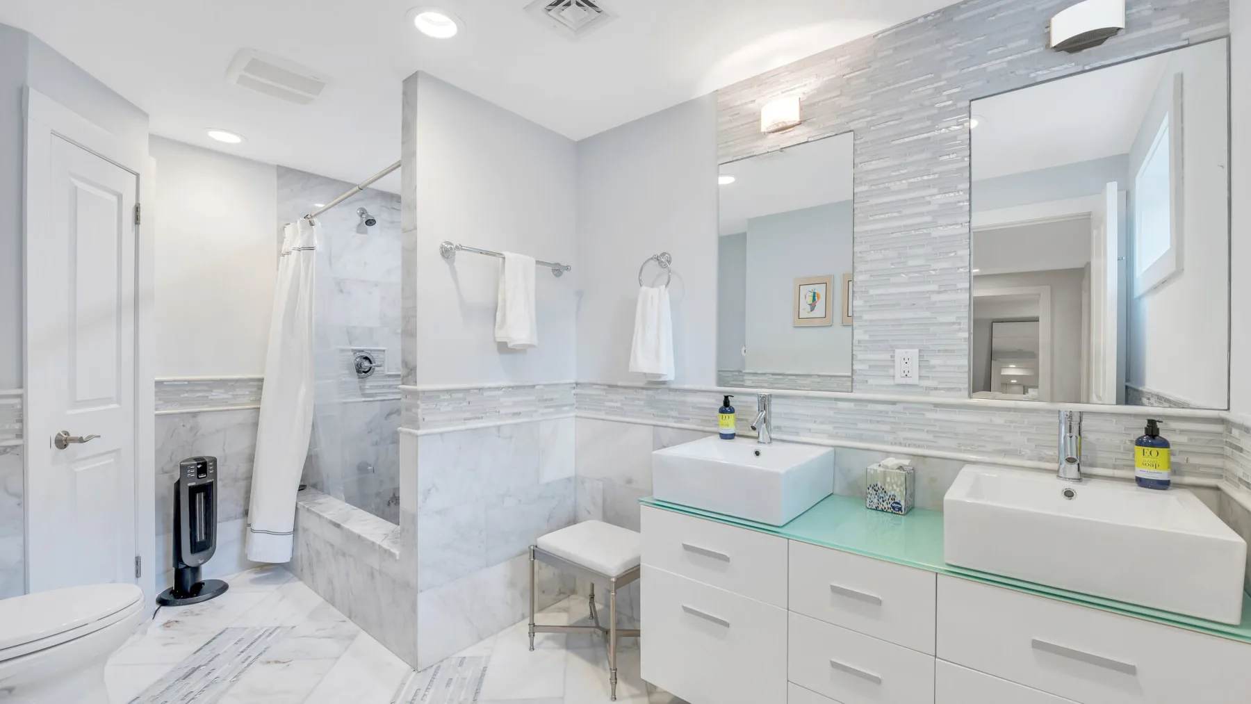 Un baño luminoso con dos lavabos, espejos y una ducha alicatada.