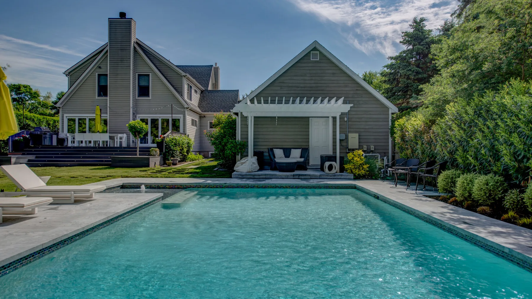 Una piscina junto a una casa gris y asientos al aire libre.