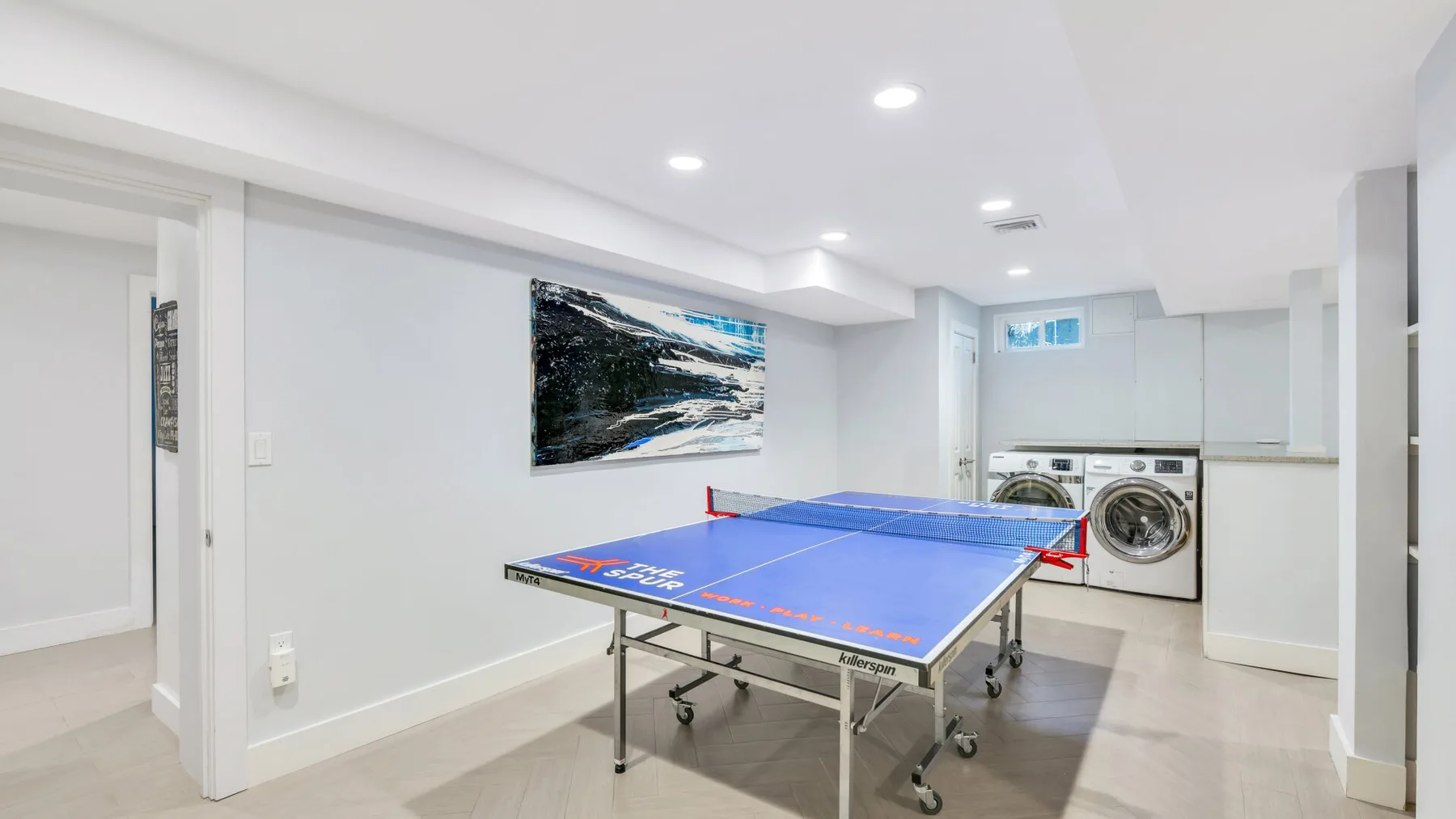 Un lavadero luminoso con una mesa de ping-pong azul frente a dos lavadoras.