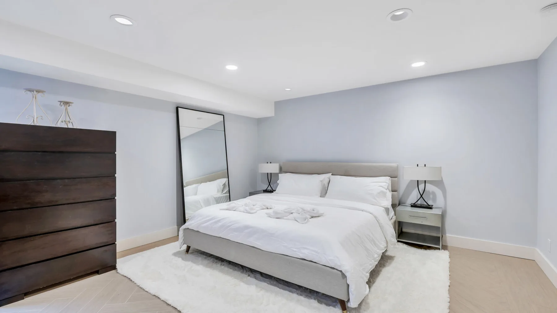 Un dormitorio luminoso con una cama, mesitas de noche y una cómoda oscura.