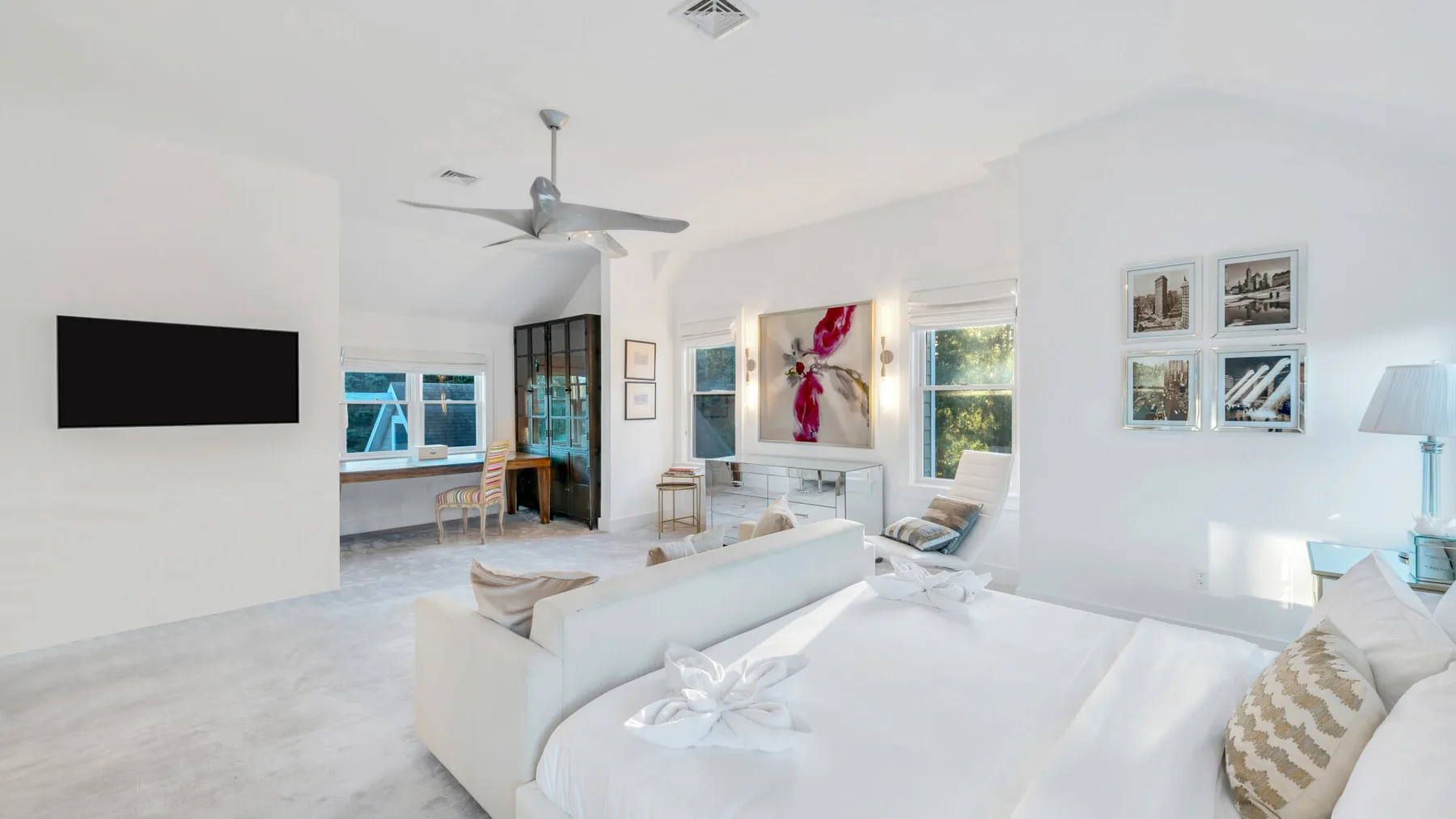 Un dormitorio luminoso con una cama grande, muebles blancos y ventanas.