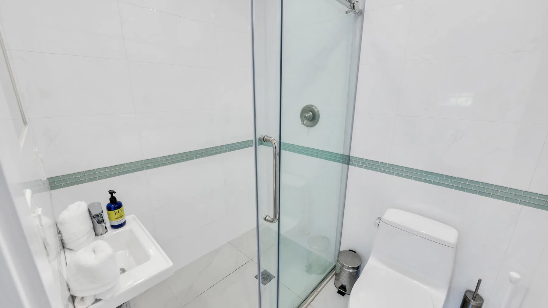 Un baño alicatado con una ducha de vidrio y un lavabo blanco.