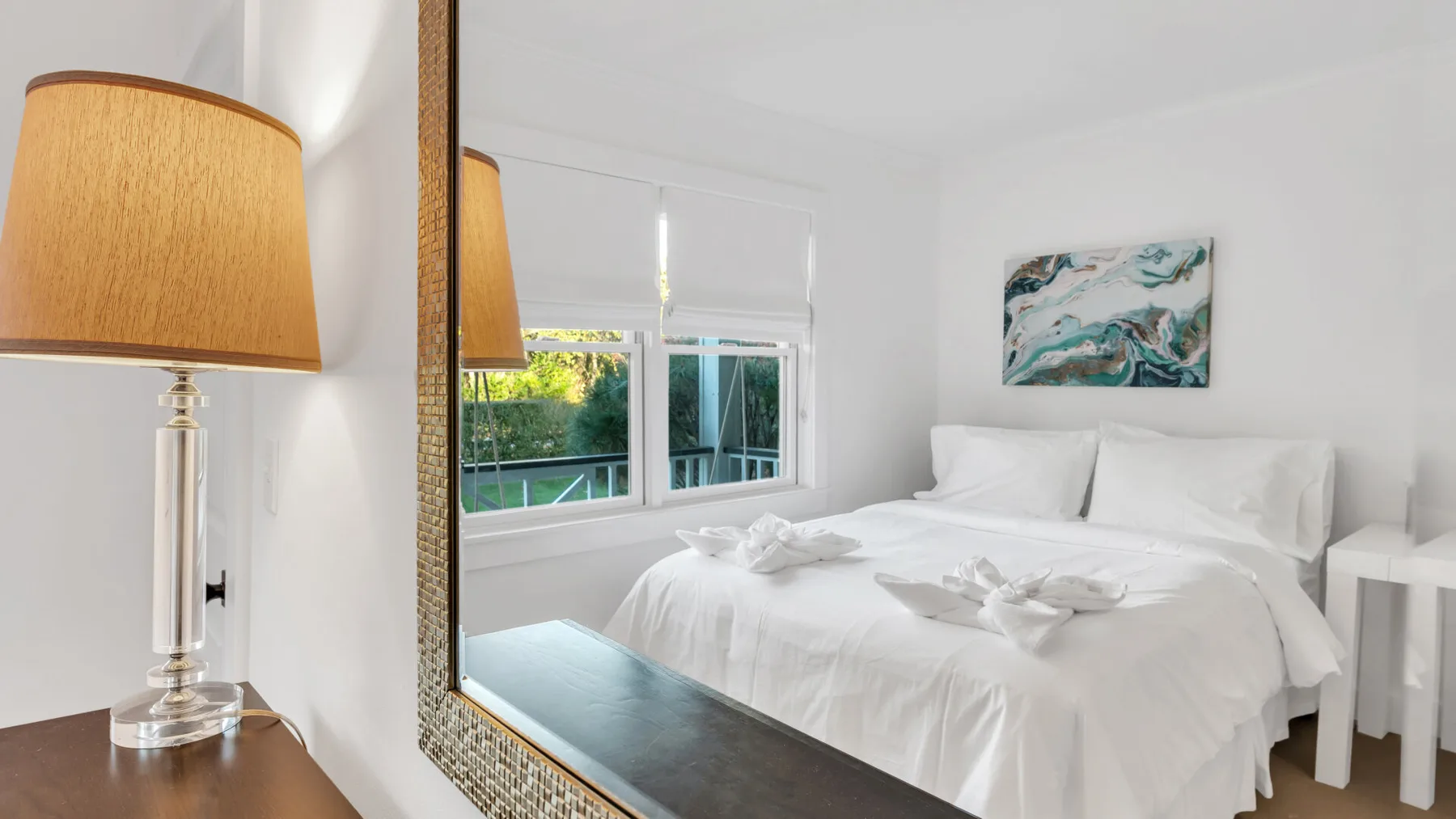Un dormitorio luminoso con una cama blanca, una ventana y arte abstracto en la pared.
