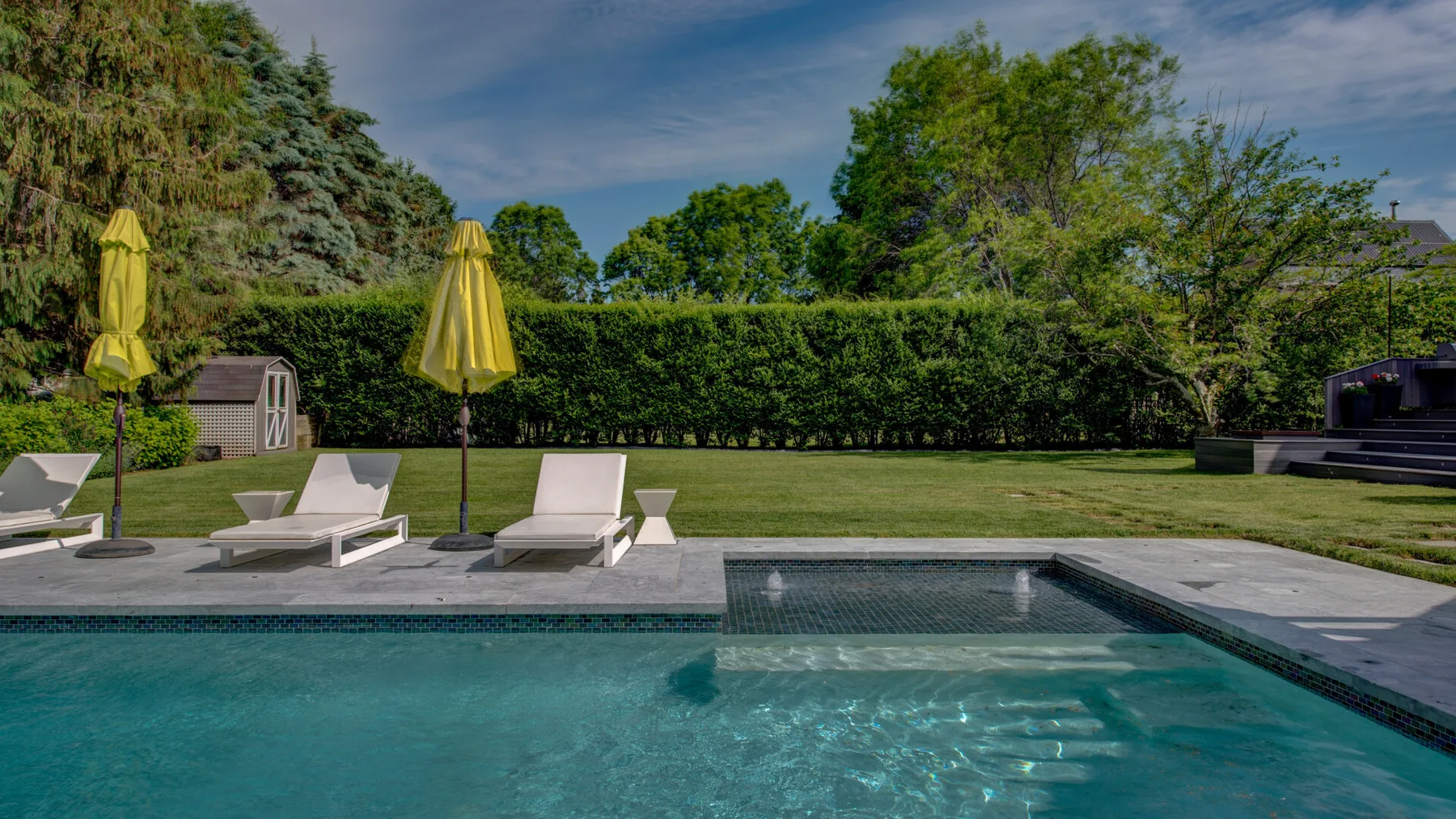 Una piscina exterior junto a un patio pavimentado y un césped verde.