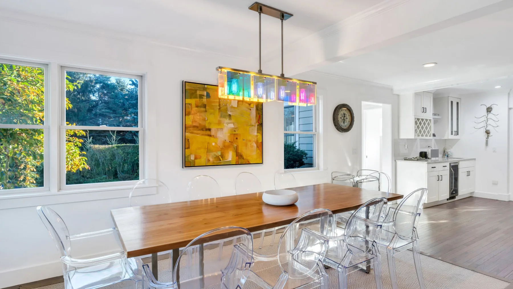 Un comedor luminoso con una mesa larga de madera y una lámpara colgante de colores.