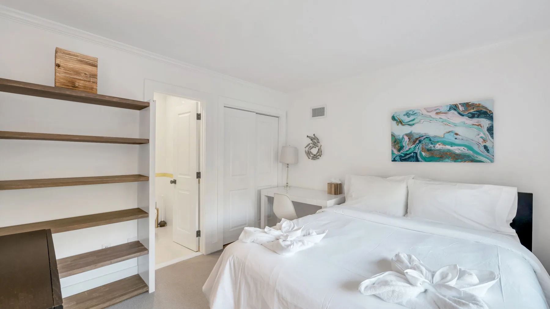 Un dormitorio luminoso con una cama tendida y estantes de madera abiertos.