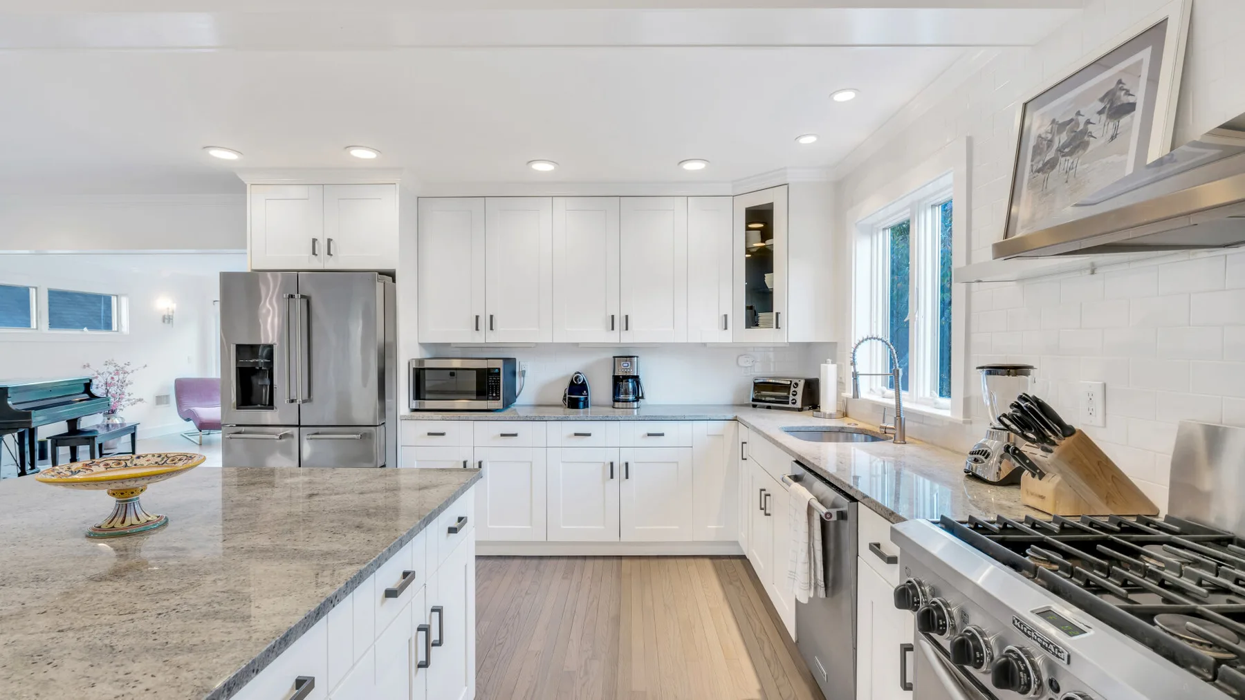 Una cocina luminosa con gabinetes blancos, encimeras de piedra y electrodomésticos de acero inoxidable.