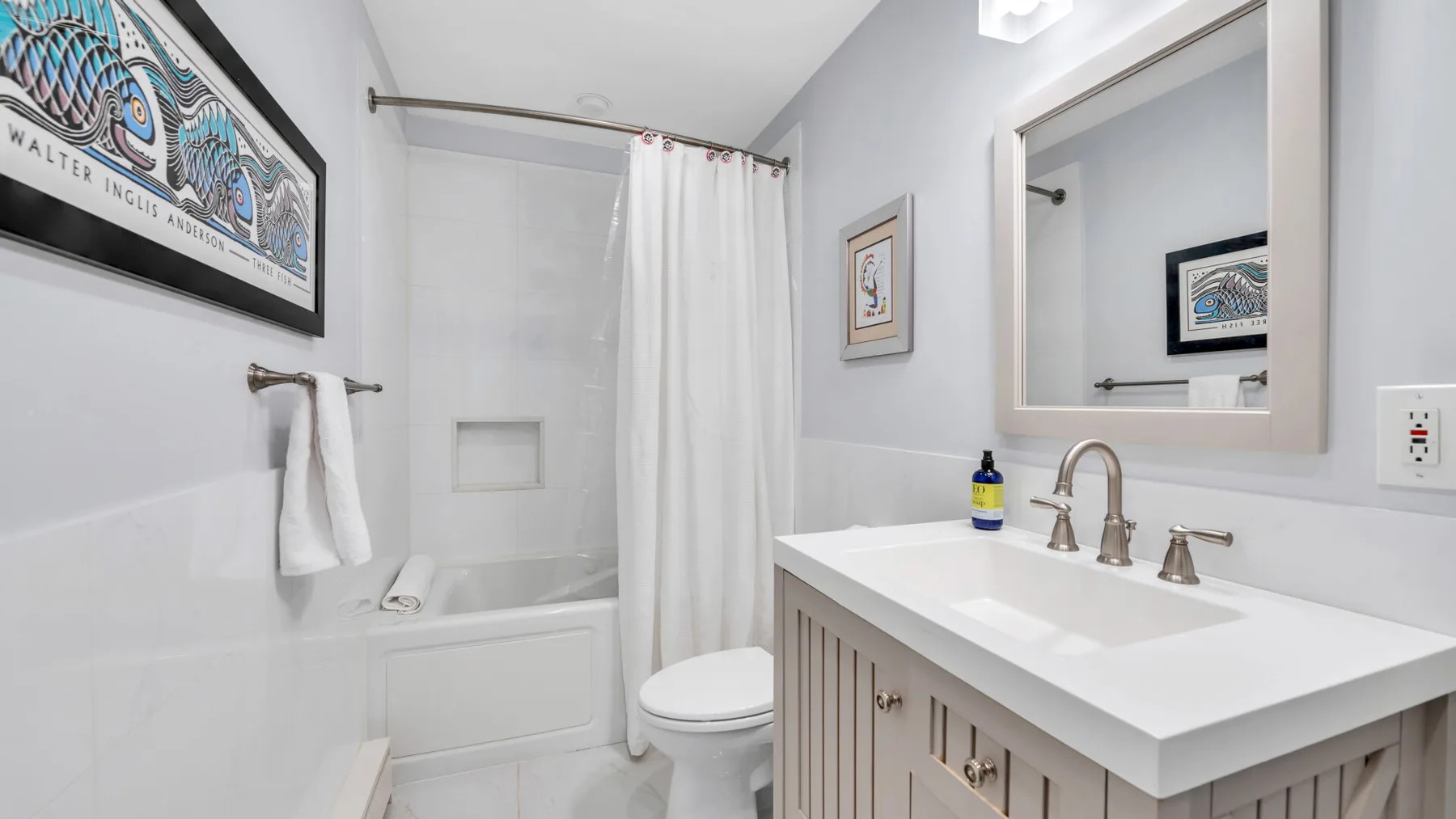 Un baño luminoso con bañera, cortina de ducha, inodoro y lavabo con mueble.