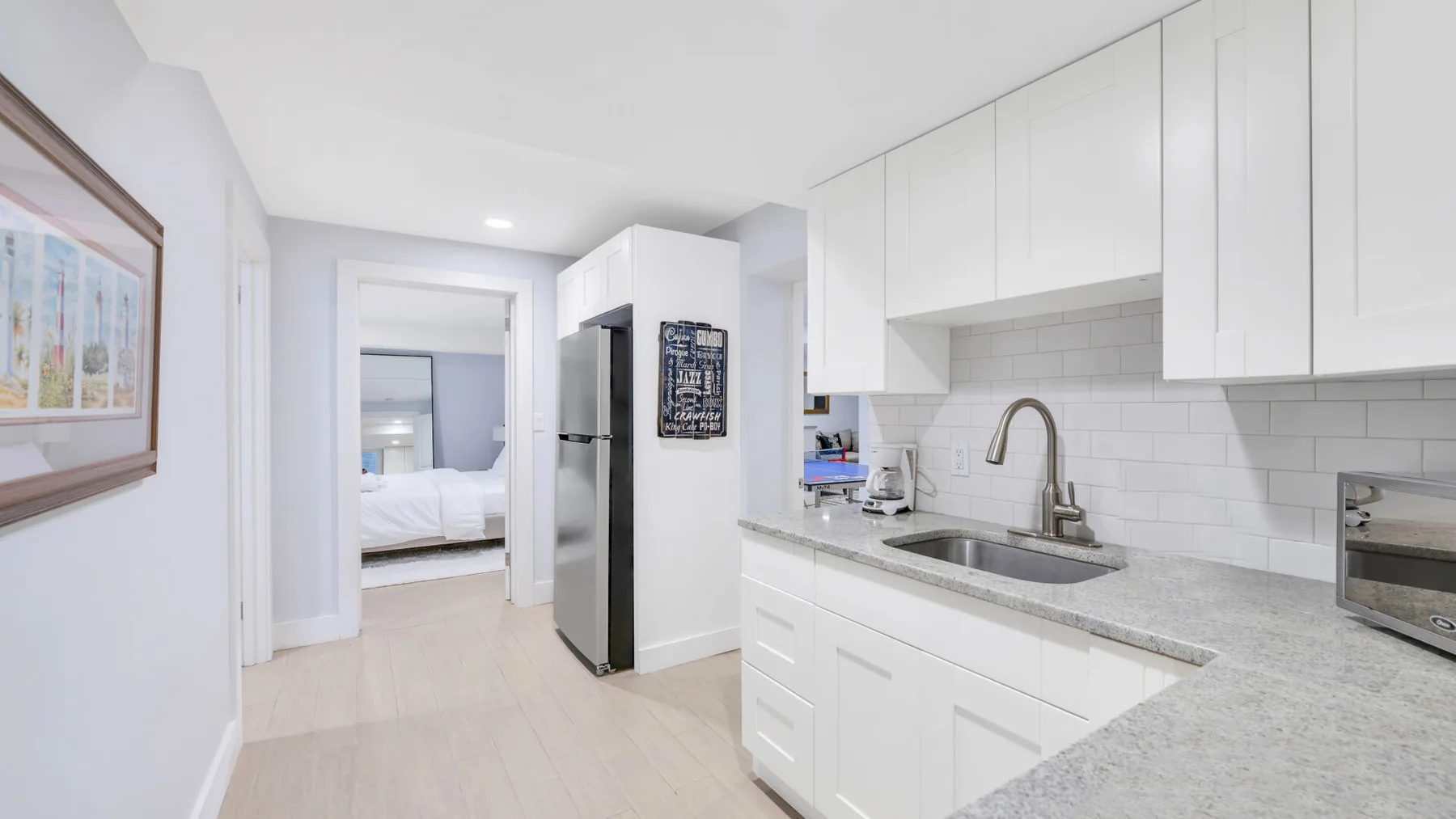 Una cocina blanca y luminosa con una encimera larga y una puerta a un dormitorio.