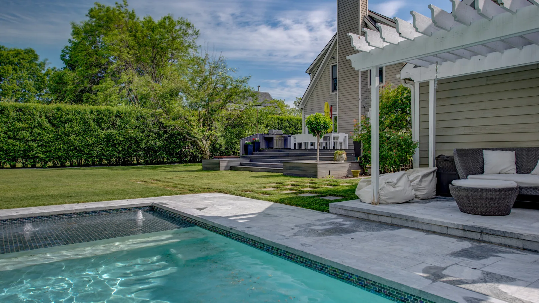 Una piscina exterior junto a un patio con asientos y una pérgola.