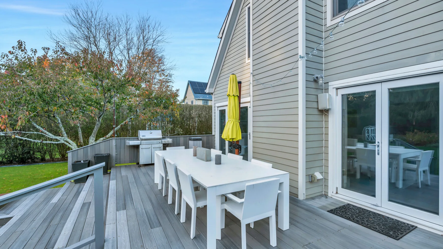 Una terraza exterior junto a una casa tiene una mesa de comedor larga y sillas.