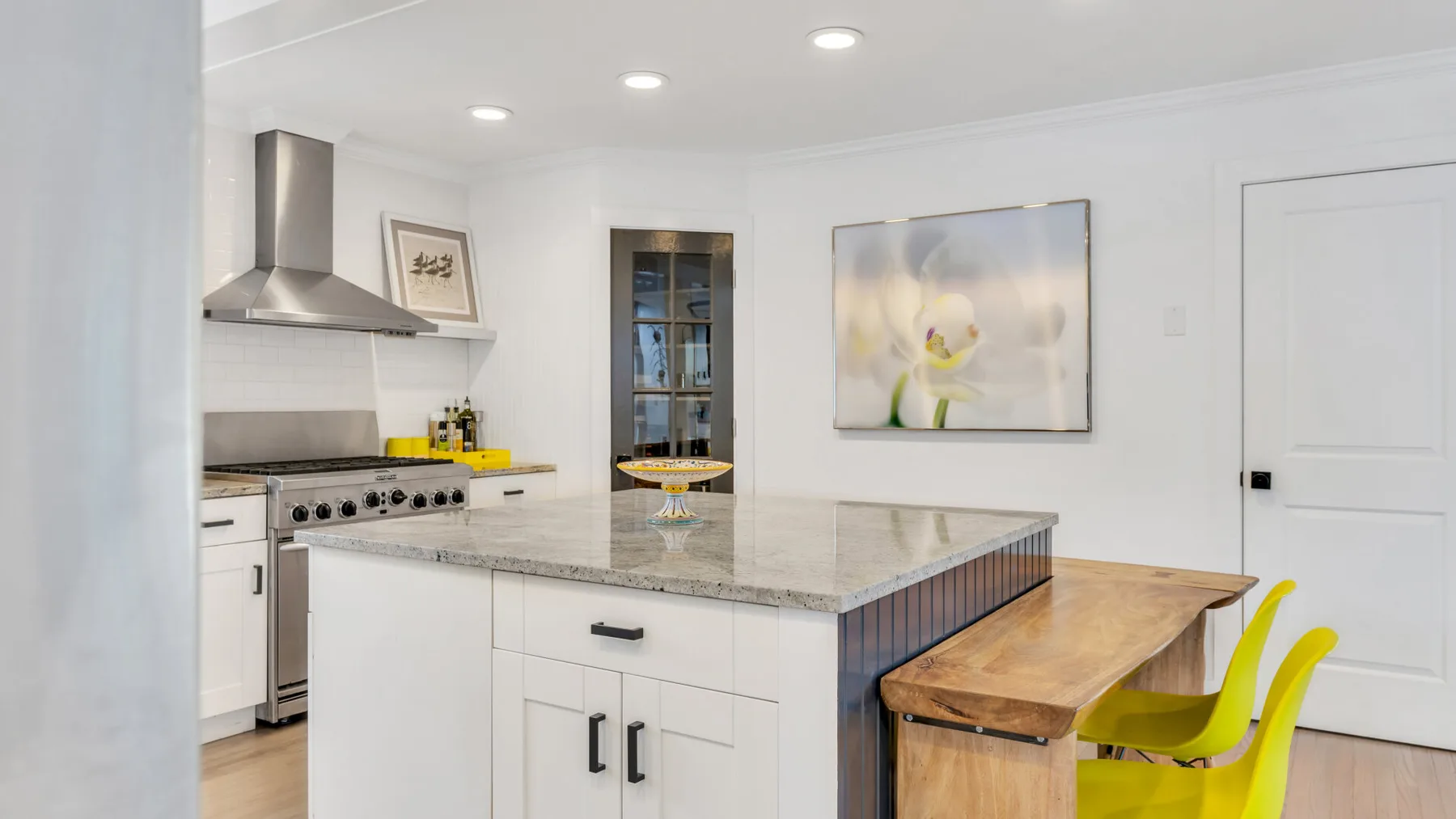 Una cocina blanca y luminosa con una isla central y taburetes de colores.