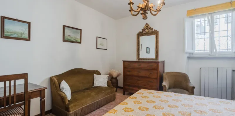 A bedroom with a bed, seating, a dresser, and a window.