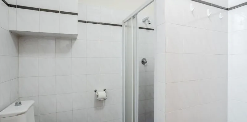 Un baño con azulejos, una ducha y un portarrollos fijado a la pared.