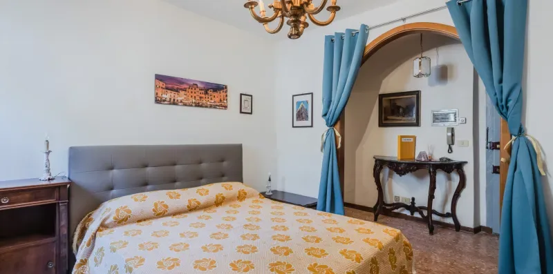A bedroom with a bed beneath a framed picture and an arched doorway.