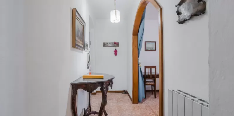 A narrow hallway with a wooden console table and an arched doorway.