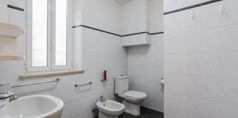 A tiled bathroom with a sink, toilet, bidet, and window.