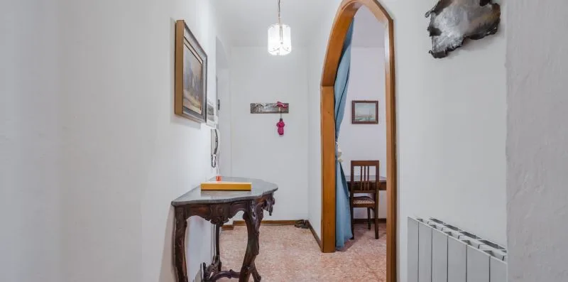 A narrow hallway with a wooden console table and an arched doorway.
