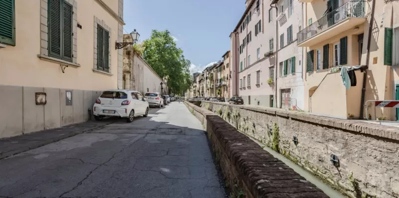 A narrow street runs between residential buildings beside a stone-lined canal.