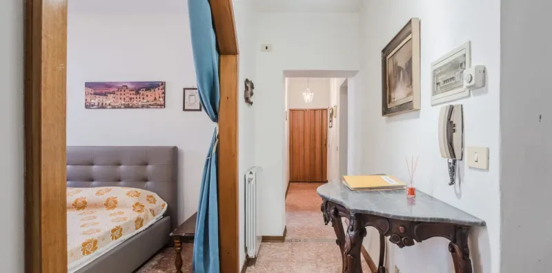 A bedroom and adjoining hallway, with a bed and a narrow console table.