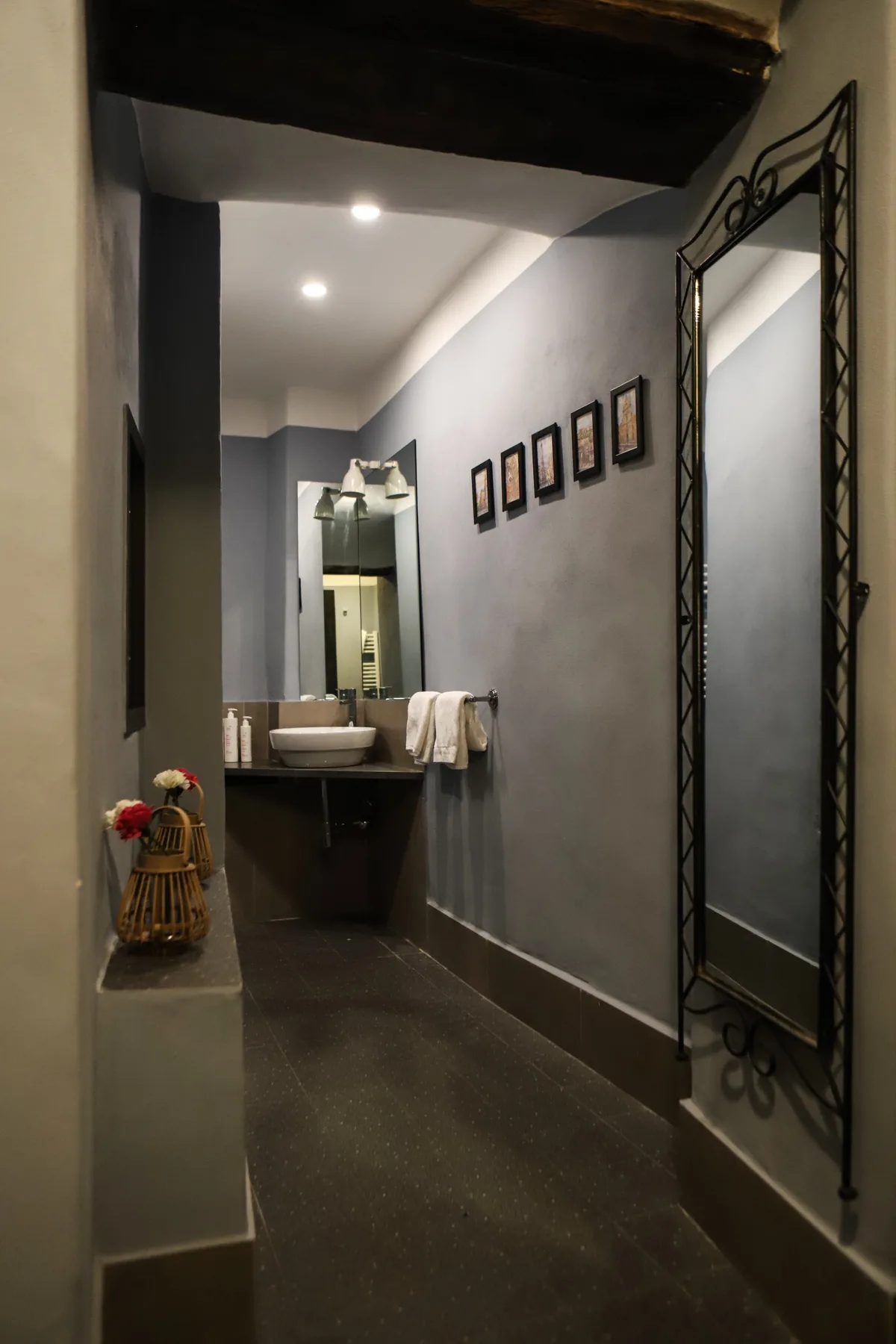 Un pasillo estrecho de baño conduce a un lavabo y un espejo, con cuadros en la pared.