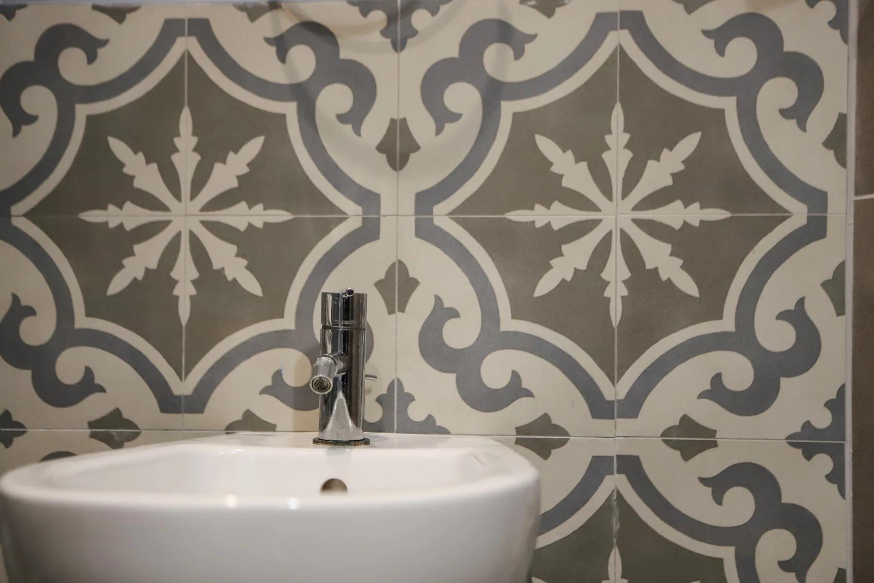 Un lavabo blanco está frente a una pared de azulejos estampados.