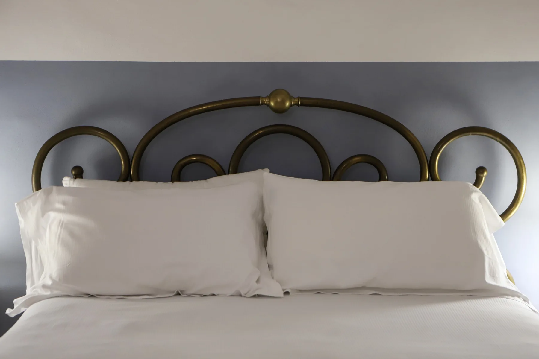 Dormitorio con almohadas blancas apoyadas contra un cabecero metálico curvo.