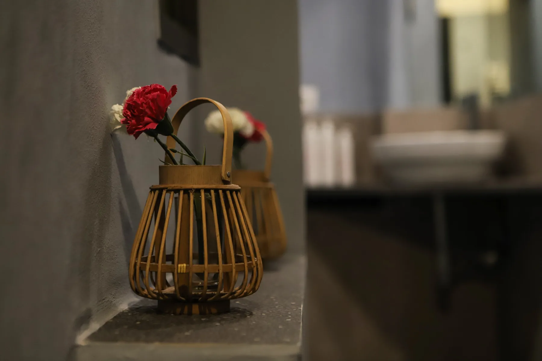 Un arreglo floral en una cesta decorativa está sobre un estante junto a un baño.