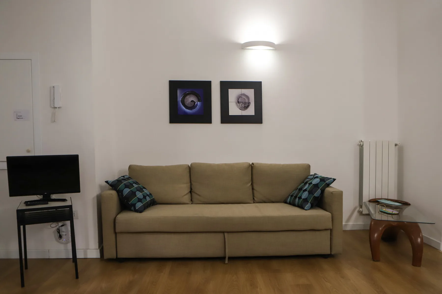 Una sala de estar con un sofá beige, cuadros y un televisor.