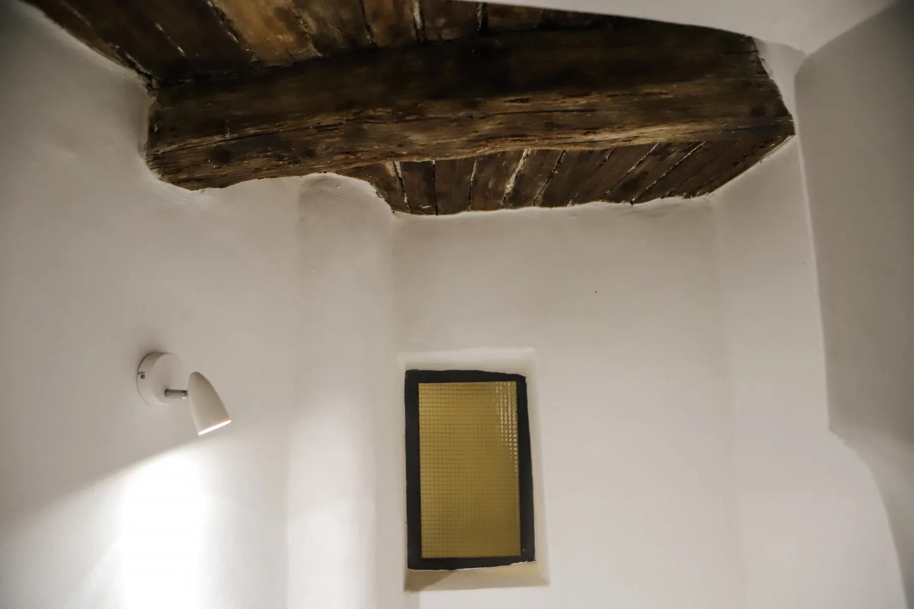 Una habitación de paredes blancas con una viga de madera oscura a la vista y un cuadro pequeño.